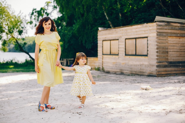 노란 모래와 맑은 해변에서 엄마는 노란 드레스와 그녀의 작은 예쁜 여자를 산책