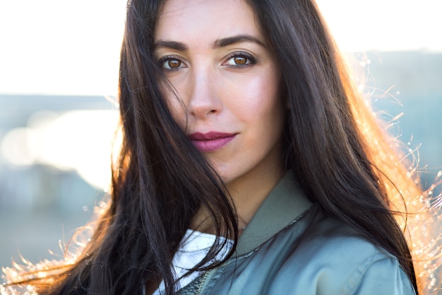 Sunny portrait of stunning young woman, long brunette hairs, trendy hat nd jacket, cold spring autumn time.