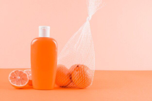 Sunscreen lotion bottle and grapefruits on colored backdrop