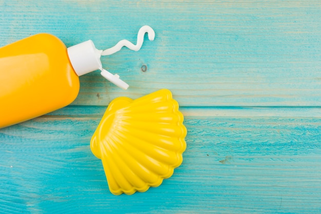 Sunscreen lotion bottle and plastic yellow scallop on turquoise wooden desk