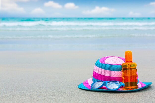 Sunscreen lotion and dark glasses with hat on the beach for summ