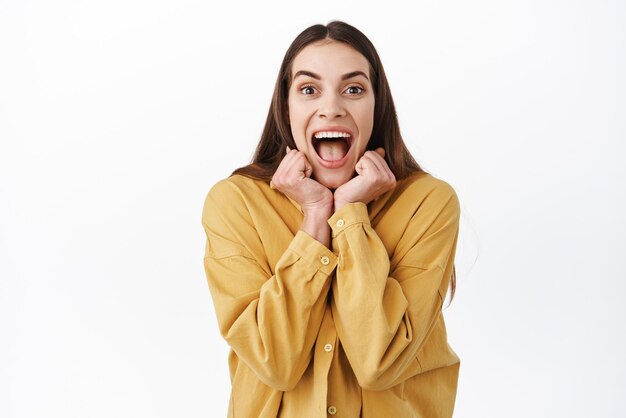 Super excited young woman screaming from joy and amazement shouting overjoy rejoicing and celebrating looking astonished at something awesome standing over white background