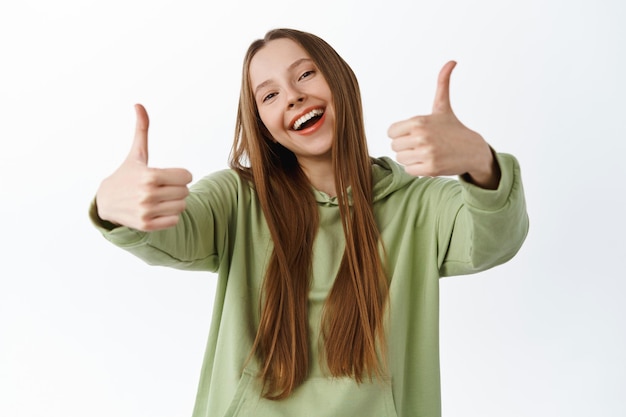 Super good. Smiling beautiful girl shows thumbs up and nod in approval, praise cool nice item, compliment great deal, agree and approve, like it, standing over white background