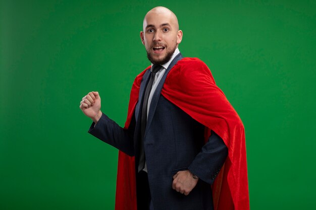 Super hero bearded business man in red cape rush running with clenched fists ready to help standing over green wall