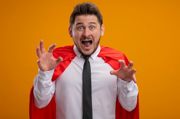 Бесплатное фото Бизнесмен супергероя в красной накидке с поднятыми руками кричит от возбуждения, стоя над оранжевой стеной