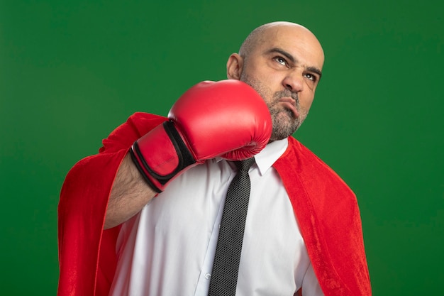 Free photo super hero businessman in red cape and in boxing gloves punching himself