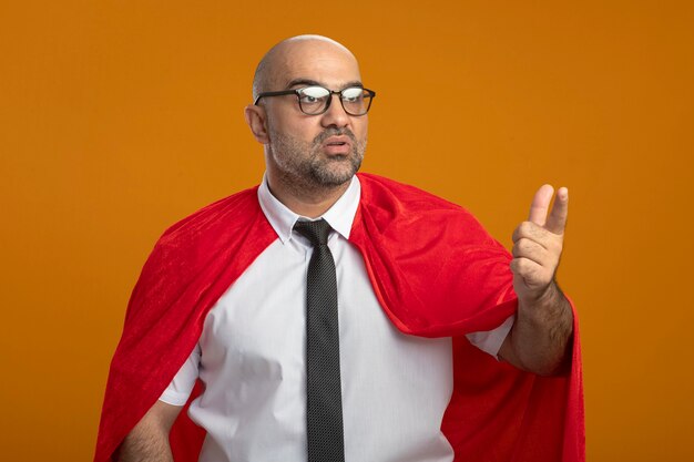 Free photo super hero businessman in red cape and glasses looking aside confused pointing at something with index figner