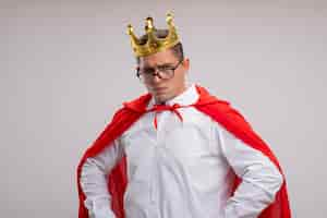 Free photo super hero businessman in red cape and glasses wearing crown  with serious face with arms at hip standing over white wall