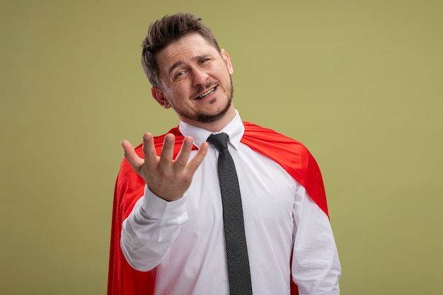 Super hero businessman in red cape looking at camera with arms out smiling with happy face standing over green background