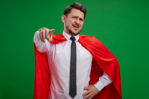 Free photo super hero businessman in red cape pointing with index finger  smiling confident standing over green wall