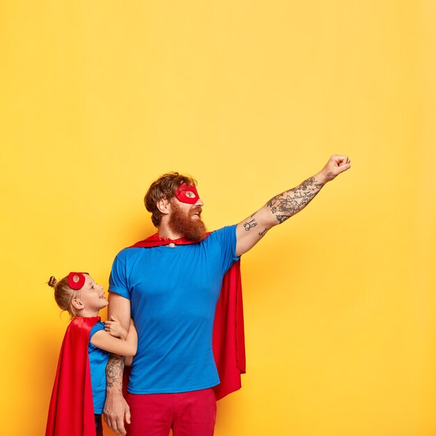 Superhero man spends leisure time with small child, makes flying gesture, raises fist