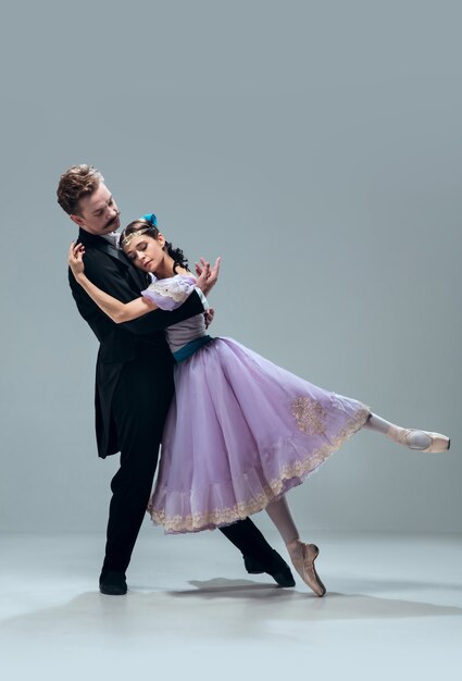 Supporting. Beautiful contemporary ballroom dancers isolated on grey studio background. Sensual proffessional artists dancing walz, tango, slowfox and quickstep. Flexible and weightless.