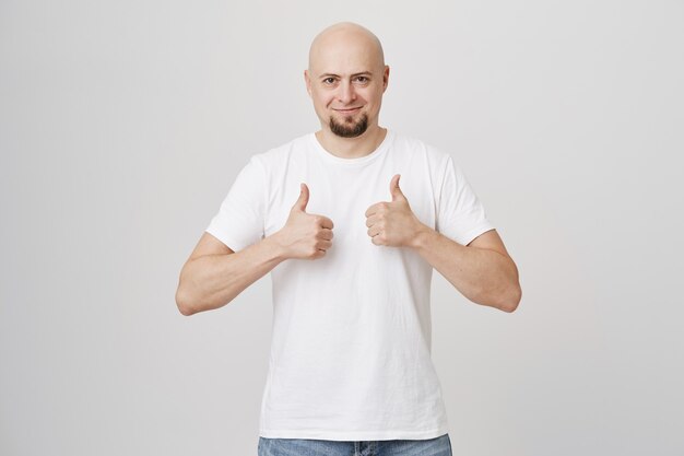 Supportive bald adult man with beard showing thumb-up in approval