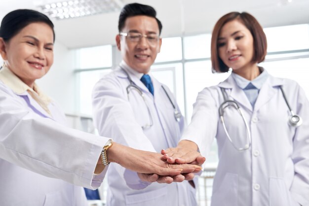 Поддерживающие медицинские коллеги складывают руки, чтобы показать сотрудничество - ключ к успеху