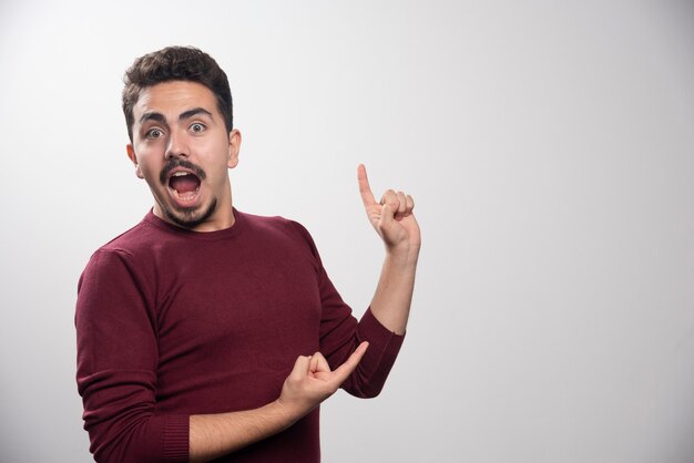 A suprised brunette man showing a finger up.