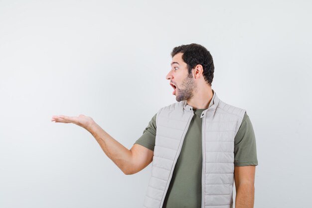 The suprised young man is pointing to left with hand on white background