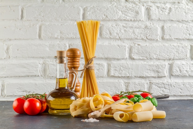 Free photo surface with different types of pasta, tomatoes and oil