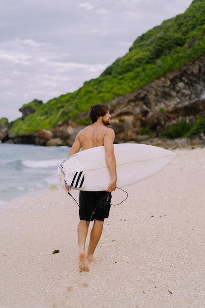 Concetto di oceano tropicale di sport all'aperto del surfista della tavola da surf. giovane uomo bello con una tavola da surf sull'oceano.