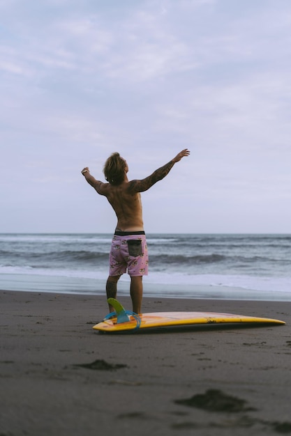 A surfer man walks with a board on a sandy beach. handsome young man on the beach. water sports. healthy active lifestyle. surfing. summer vacation. extreme sport.