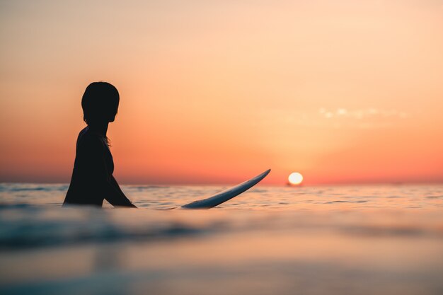 背景の空に息をのむような夕日と海のサーファー