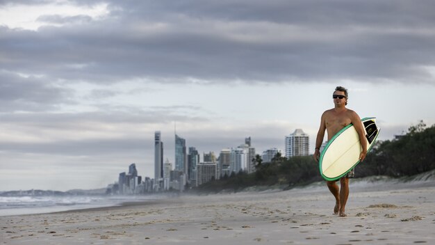 Серфер гуляет с доской для серфинга на пляже Surfers Paradise