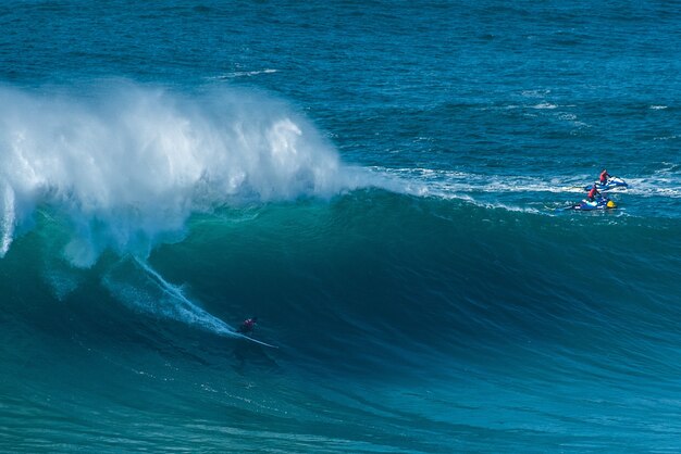 Surfers riding on the waves of the Atlantic Ocean toward the shore at Nazare, Portugal