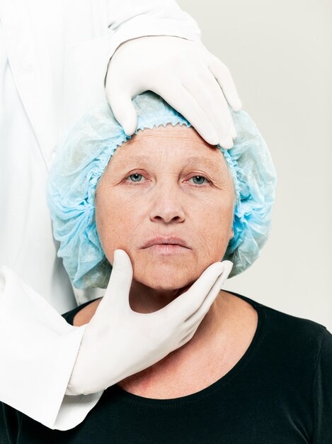 整形外科の前に中年の女性の皮膚チェックを行う外科医