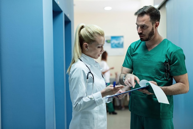Хирург и женщина-врач просматривают медицинскую карту пациента, стоя в вестибюле больницы