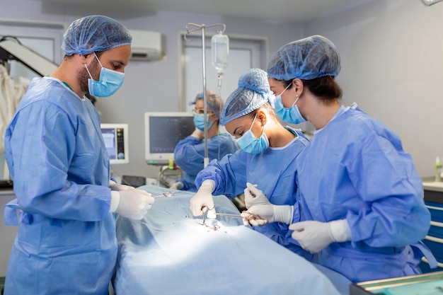 조명 장비 아래에서 작업하는 외과 남성과 여성 의사는 파란색 수술복을 입고 병원에서 일하고 있습니다