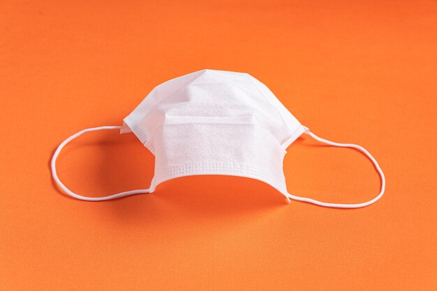 ミニマリストのオレンジ色の背景上の外科用マスク