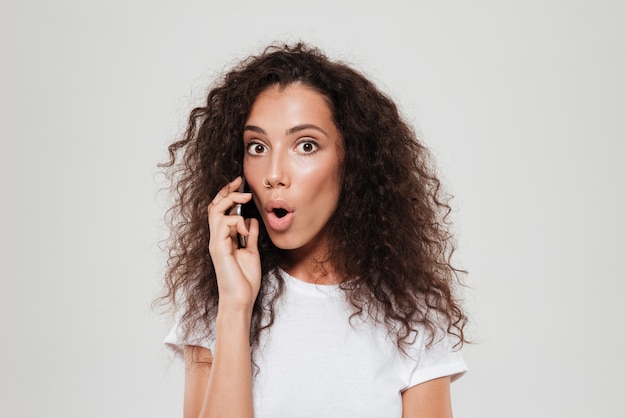 Surpised curly woman talking by the smartphone