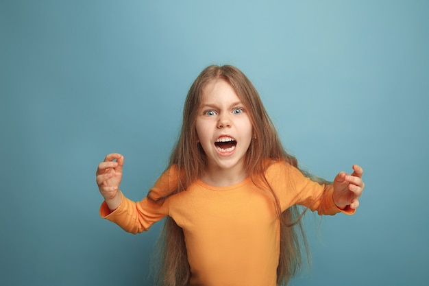 Free photo the surprise, rage. the screaming surprised teen girl on a blue studio background. facial expressions and people emotions concept. trendy colors. front view. half-length portrait