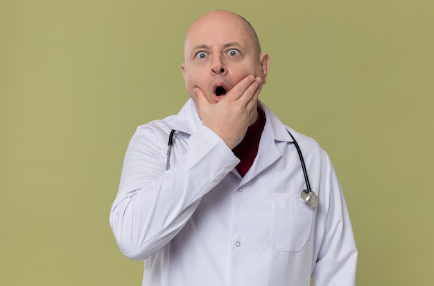 Free photo surprised adult slavic man in doctor uniform with stethoscope putting hand on his chin and