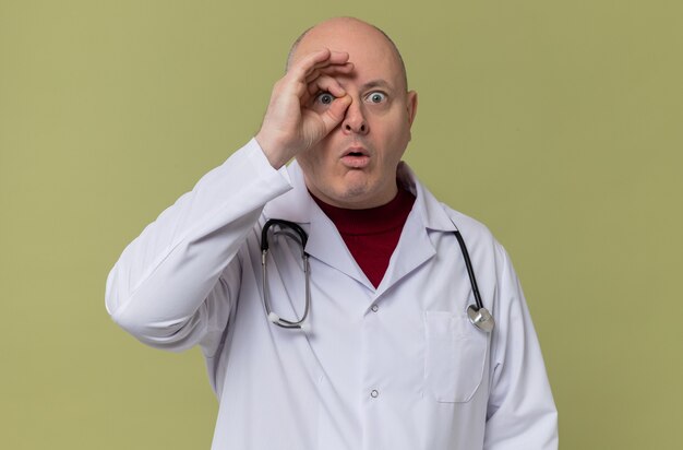 Surprised adult slavic man in doctor uniform with stethoscope through fingers 