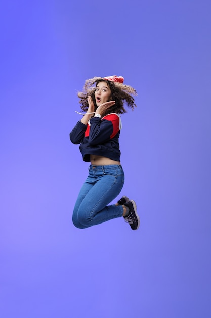 Surprised and amazed amused goodlooking woman with curly hair in winter beanie and sweatshirt open m.