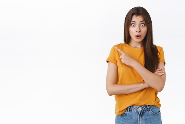 Surprised amazed goodlooking girl gossiping with friend stare amazed widen eyes folding lips say wow as pointing upper left corner heard rumor about coworker standing near white background