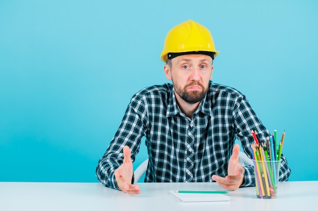 Free photo surprised architect is looking at camera by sitting on blue background