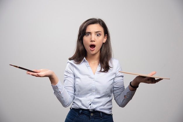 Free photo surprised artist holding paintbrush and palette over gray wall.