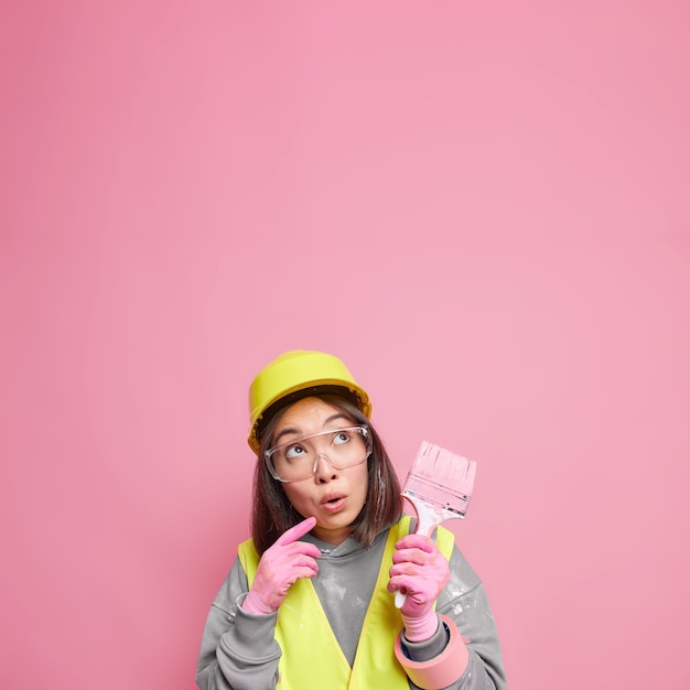 Бесплатное фото Удивленная азиатская женщина, сосредоточенная вдали, думает о ремонте квартиры, держит кисть для рисования