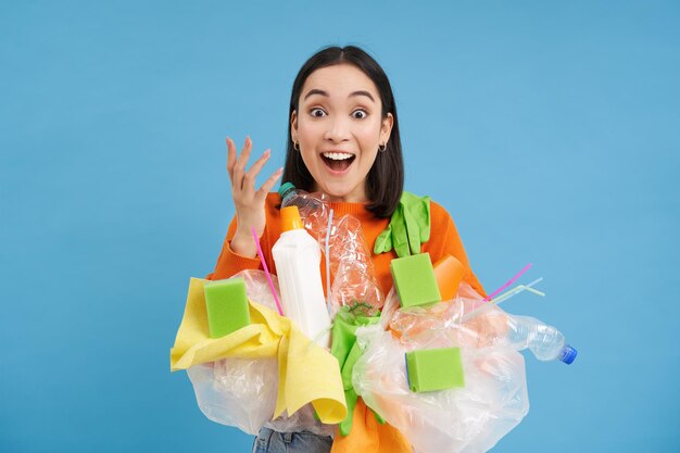 Surprised asian woman sorting garbage recycling looks excited carries plastic waste blue background