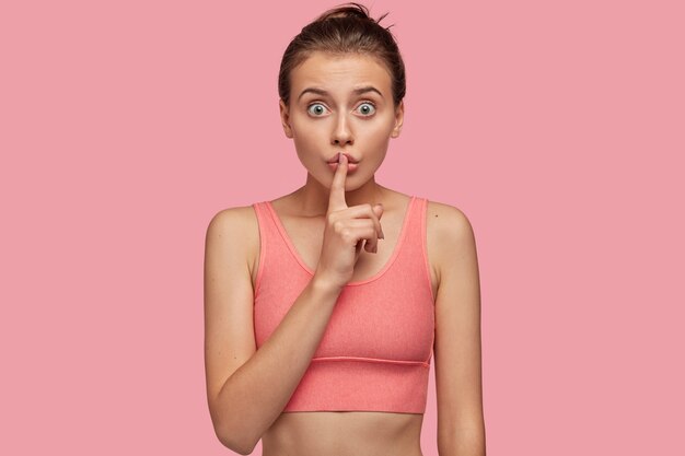 Surprised athletic woman posing against the pink wall