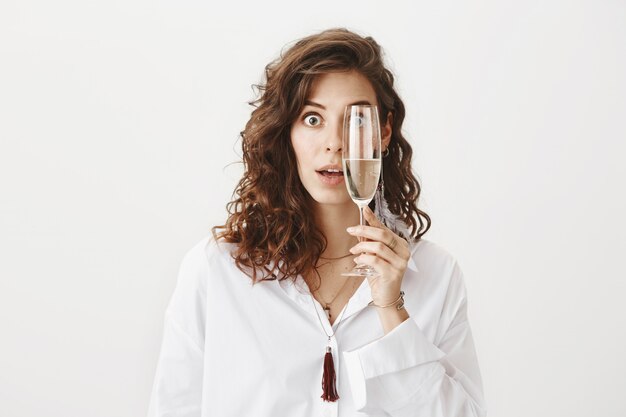Surprised attractive woman holding a glass champagne over her eye