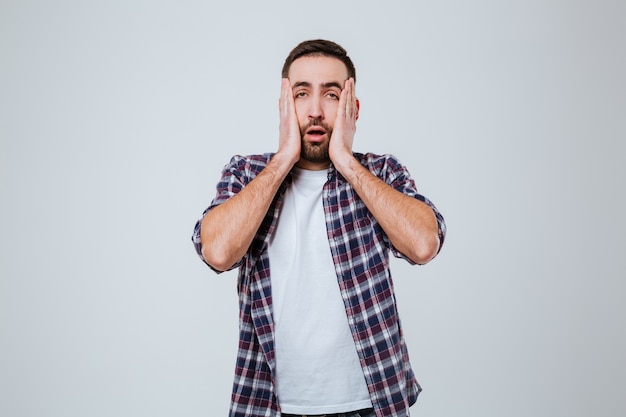 Surprised Bearded man in shirt holding his cheeks