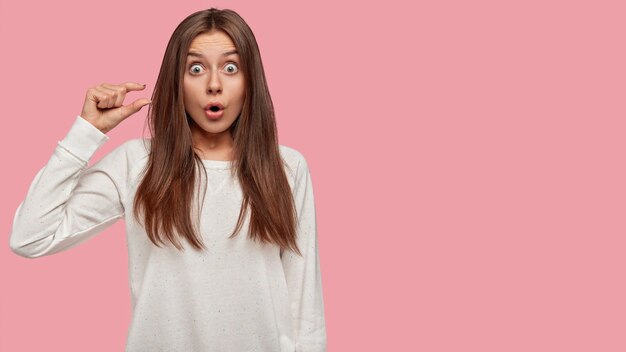 Surprised beautiful brunette posing against the pink wall