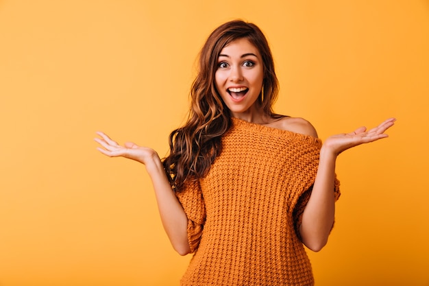 Surprised beautiful woman posing on bright yellow. Lovely brunette girl standing in studio with amazed face expression.