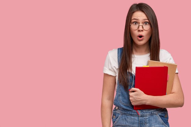 Free photo surprised beautiful young woman with asian apperance, make up, holds notebooks, wears casual outfit