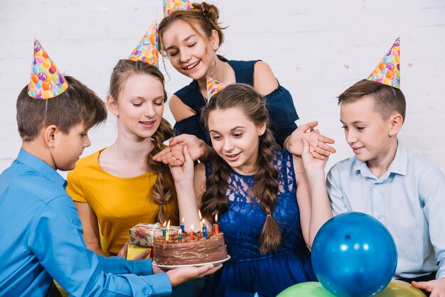 Surprised birthday teenage girl looking at cake brought by her friend