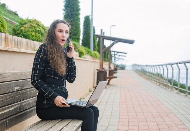 Удивленная девушка-блогер разговаривает по смартфону в парке