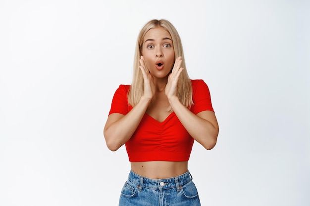 Surprised blond woman gasping amazed looking impressed at camera say wow and stare at something cool white background Copy space