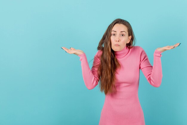 Surprised blonde girl is opening wide her hands on blue background